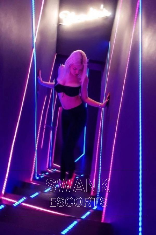 Naomi walking up stairs of nightclub in room with purple and blue LED lights wearing black lingerie 